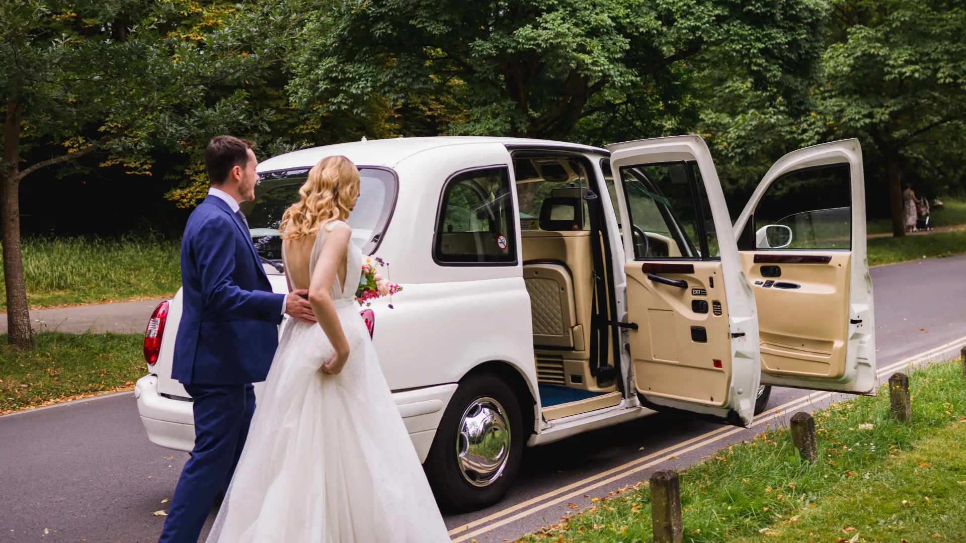 White taxi Cab at wedding in Wales with Bride and Groom walking towards the white wedding cab