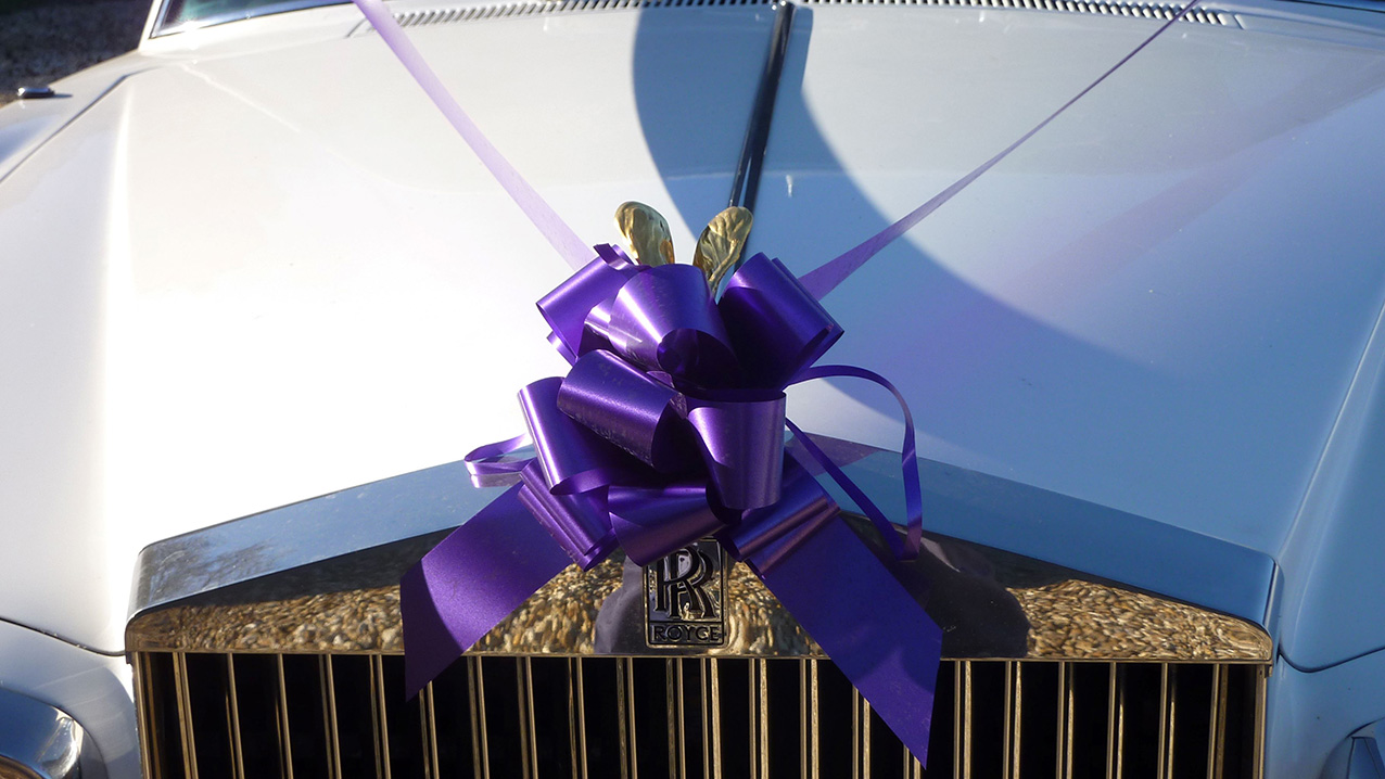 close up photo of top of Front Chrome grill with Purple ribbons and bow attached to the spirit of ecstasy