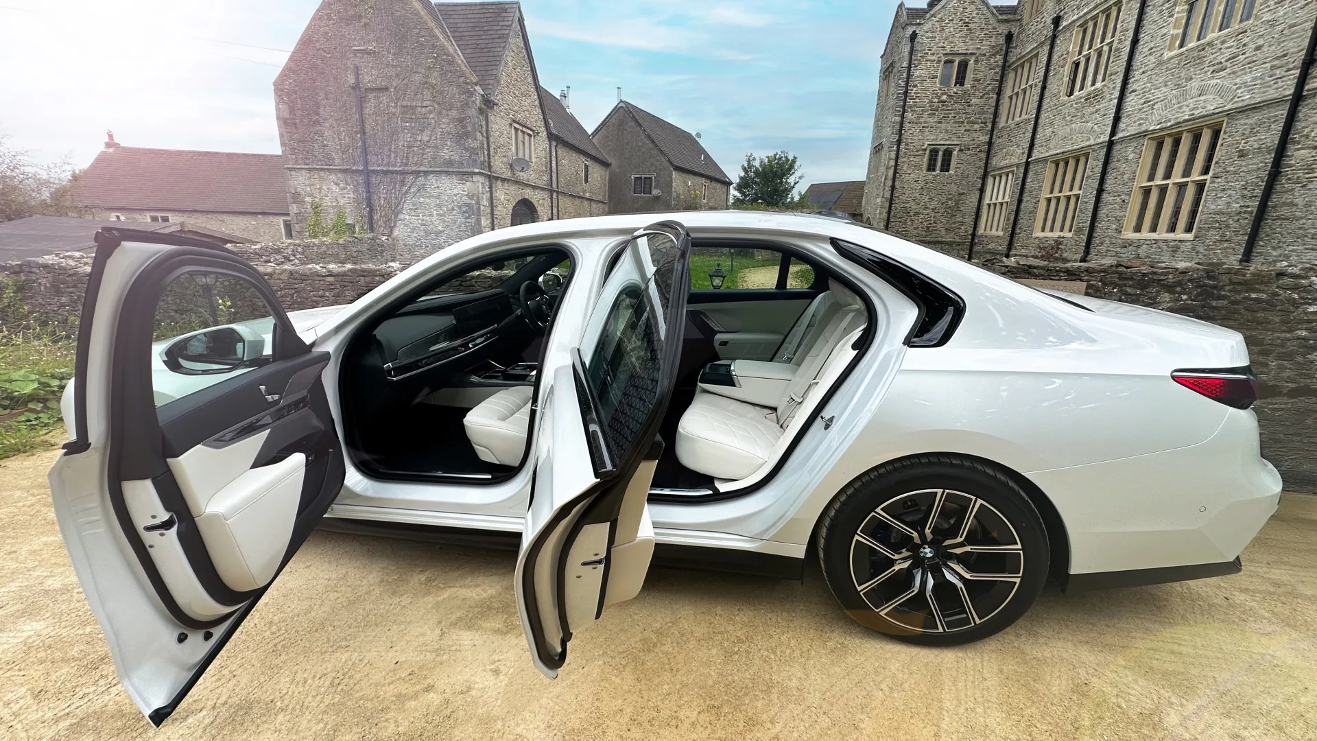 Left view of which Electric BMW i7 with both rear and front passengers doors open showing cream leather interior. Vehicle is parked in front of a church in Cardiff.