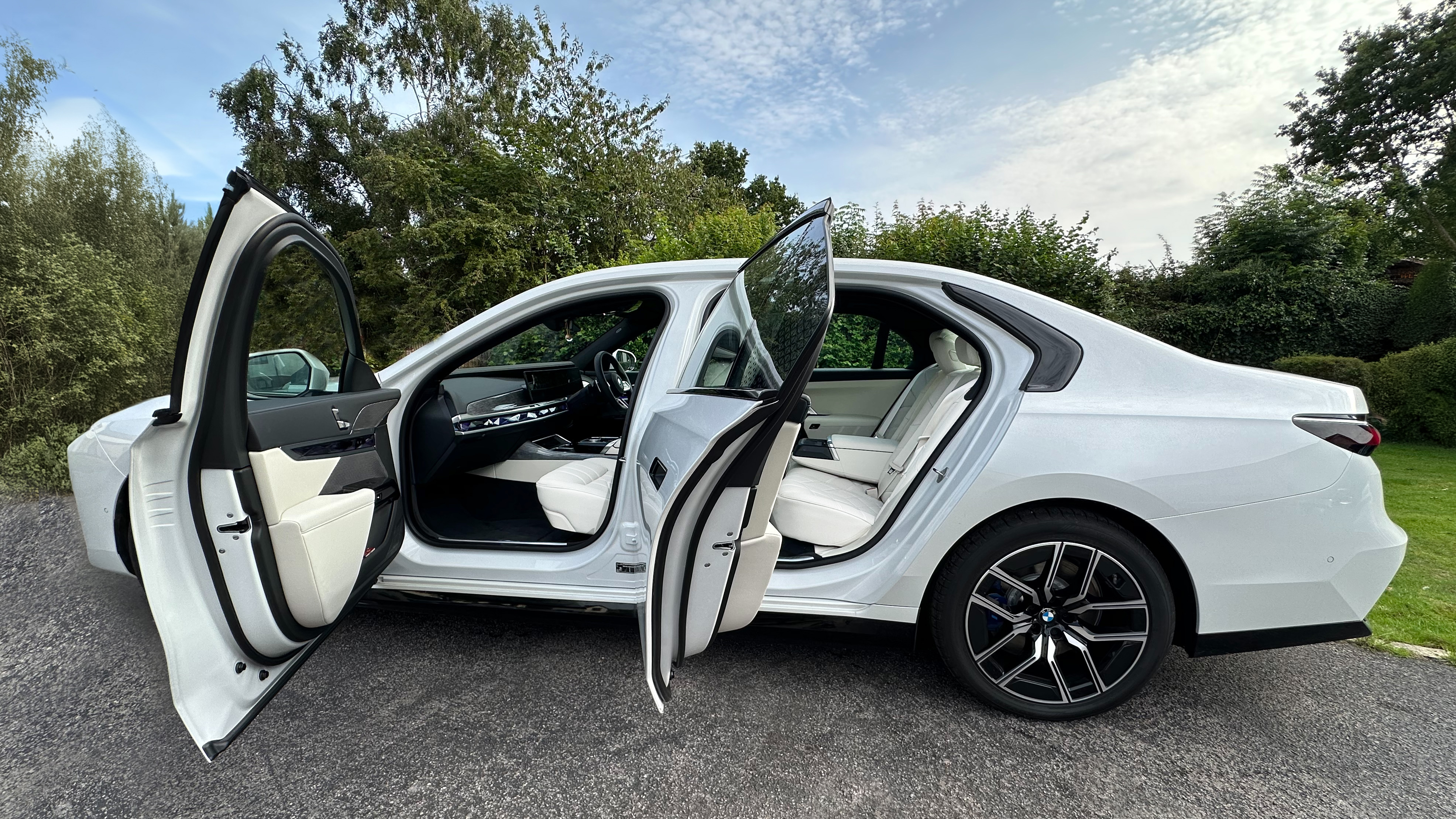 Left view of which Electric BMW i7 with both rear and front passengers doors open showing cream leather interior