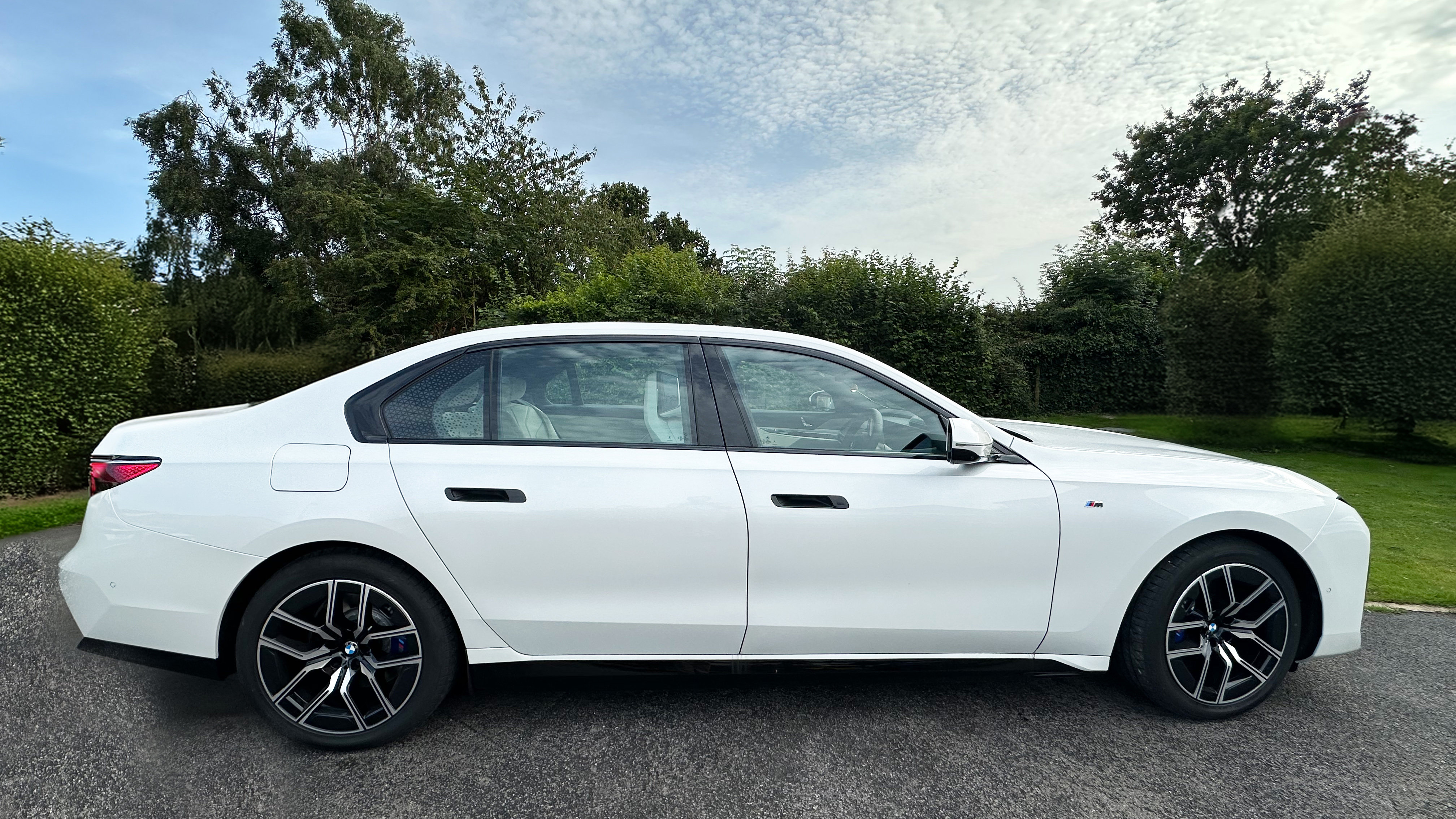 Right view of which Electric BMW i7 with Black and Silver Alloy Wheels, blue sky and green trees in the background