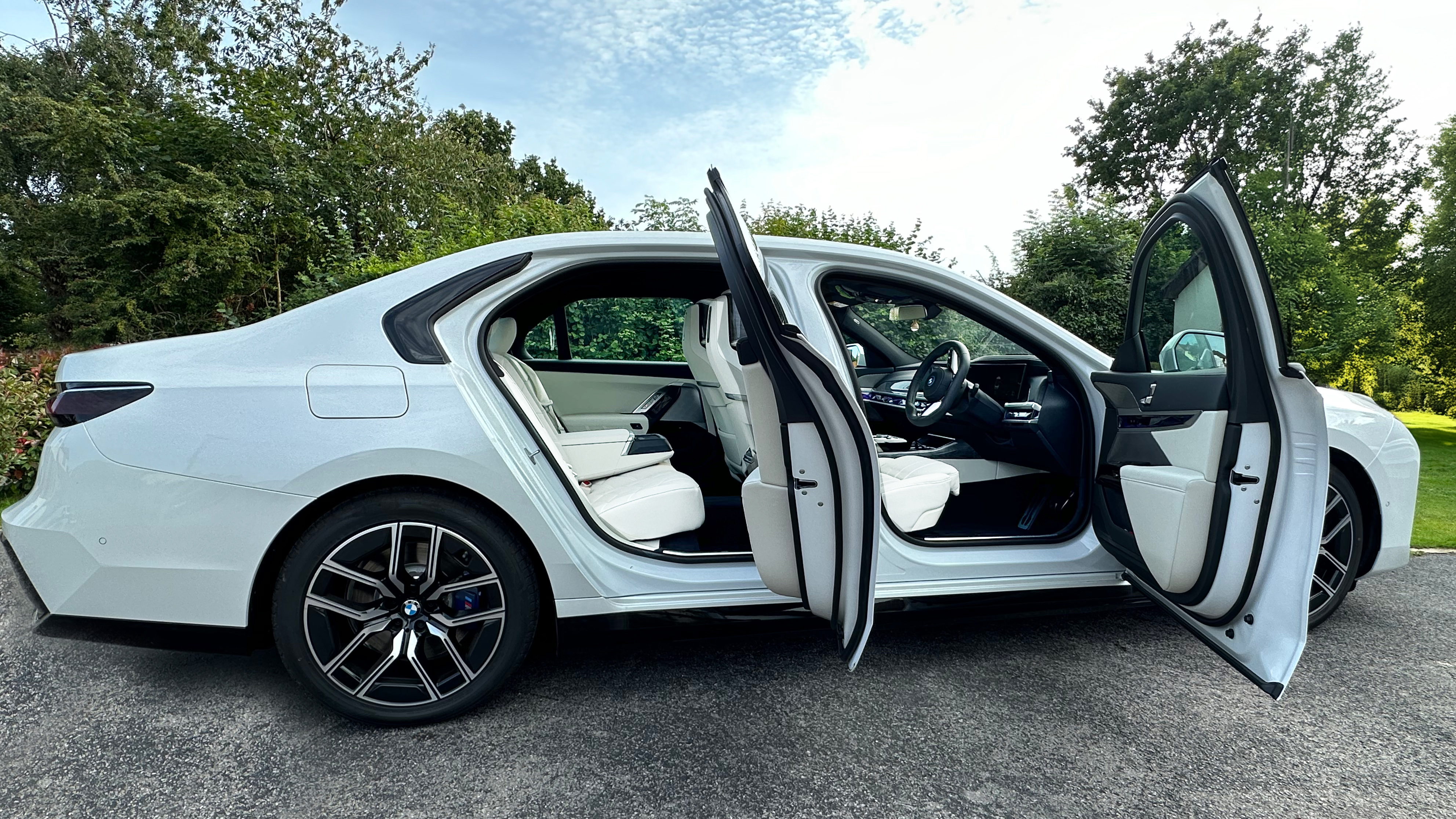 Right view of which Electric BMW i7 with both rear and front passengers doors open showing cream leather interior