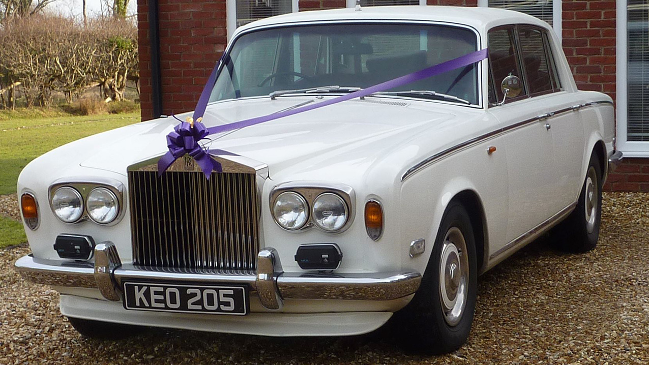 Classic Rolls-Royce Silver Shadow with chrome bumper and purple ribbon and bow across its front bonnet