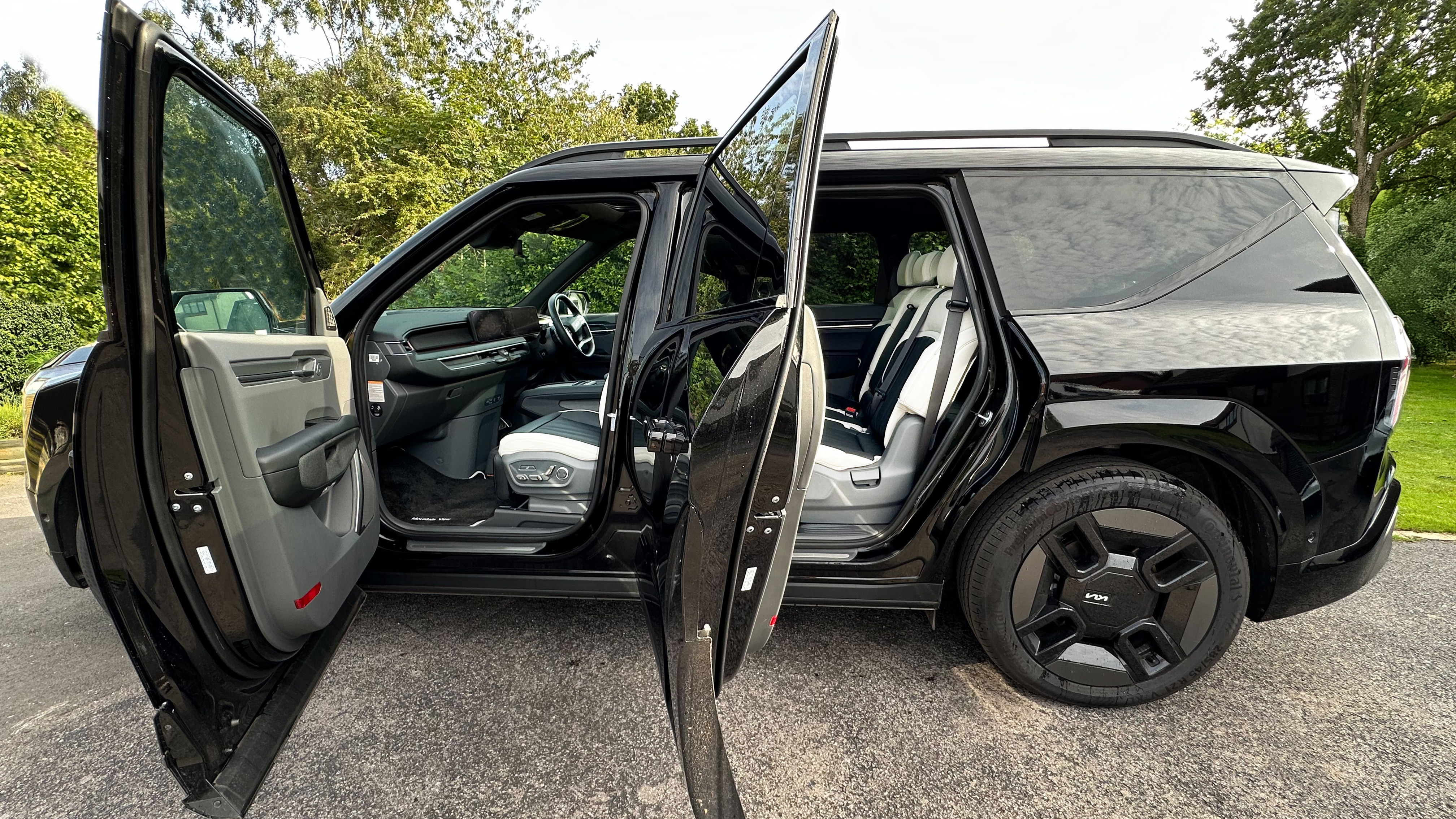 Left view of Black KIA SUV with black alloy wheels and both front and rear passenger doors are open