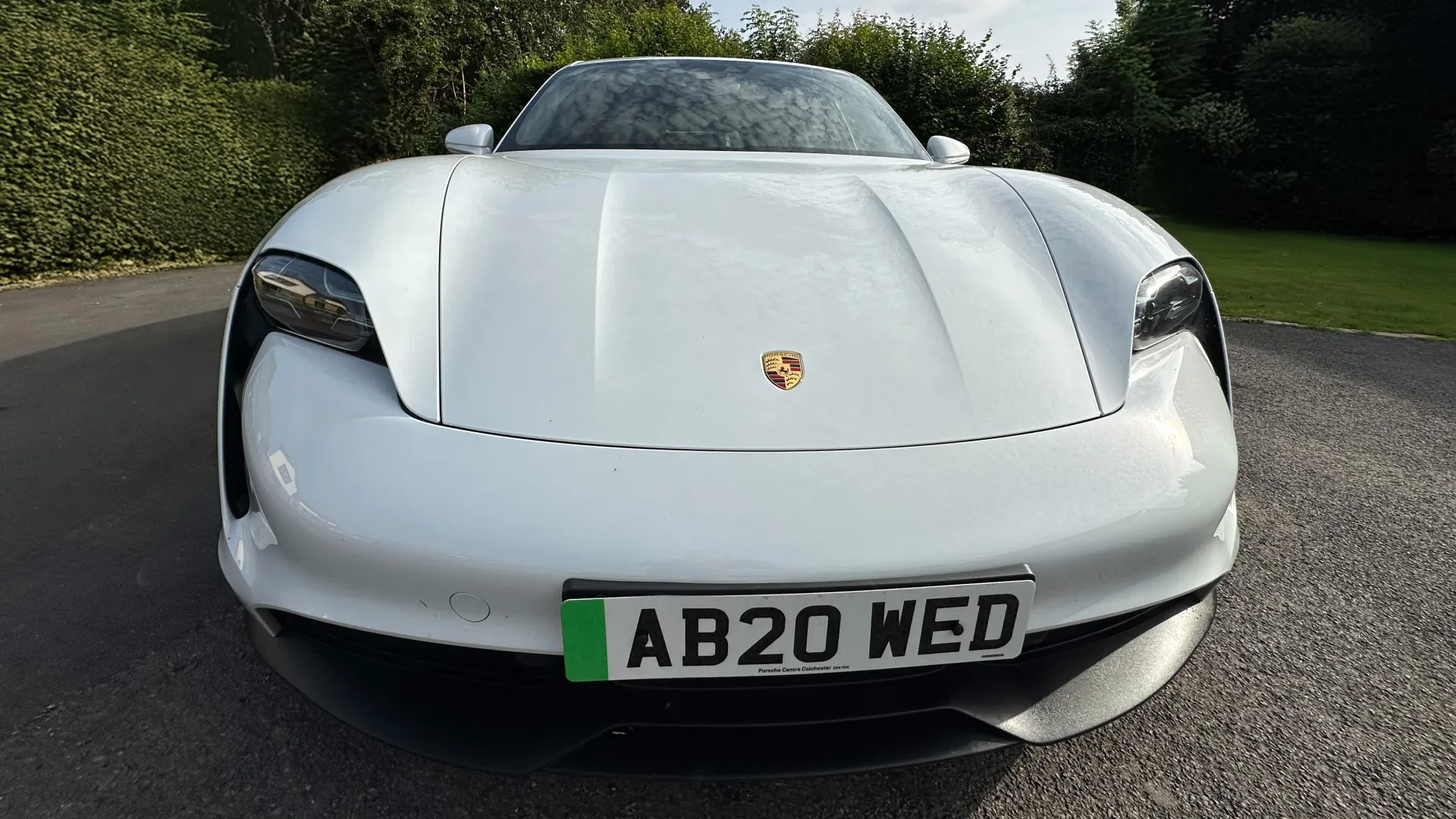 Full front view of White Porsche Taycan showing the Porsche badge