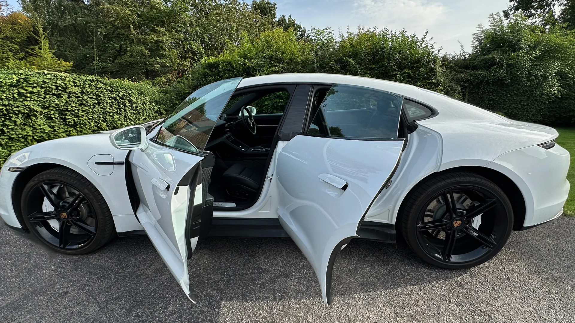 Left side view of White Porsche Taycan with black a wheels and doors open