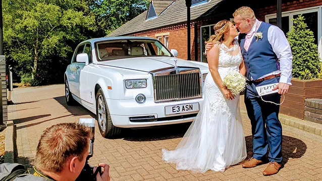 White rolls-Royce Phantom with Bride and Groom kissing in front of the vehicle.