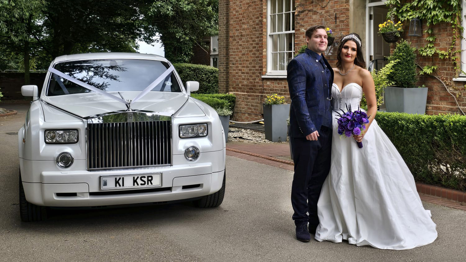 White rolls-Royce Phantom dressed with white ribbons and the newly married couple standing in front of the vehicle.