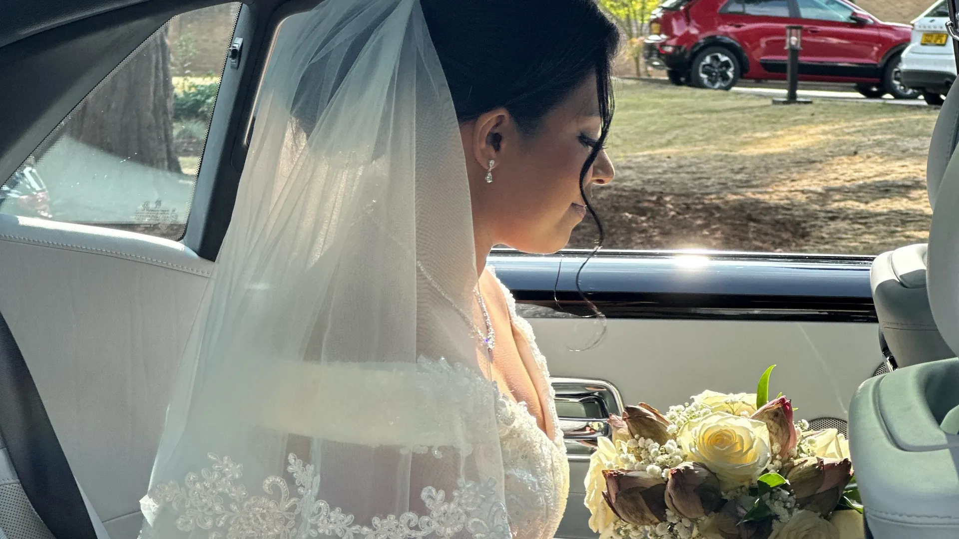 Bride holding a white rosed bouquet of flowers sitting inside car