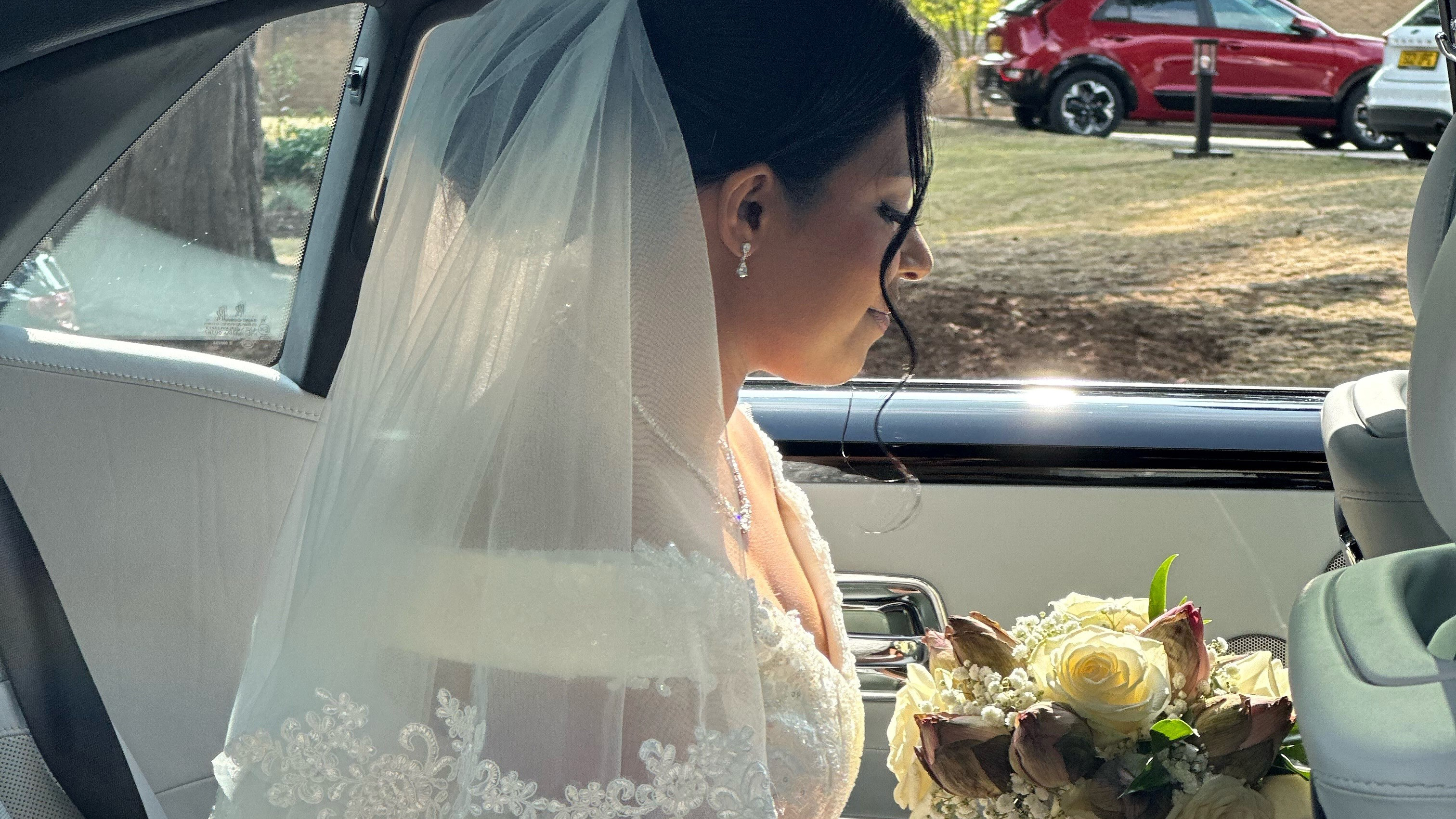 Bride holding a white rosed bouquet of flowers sitting inside car