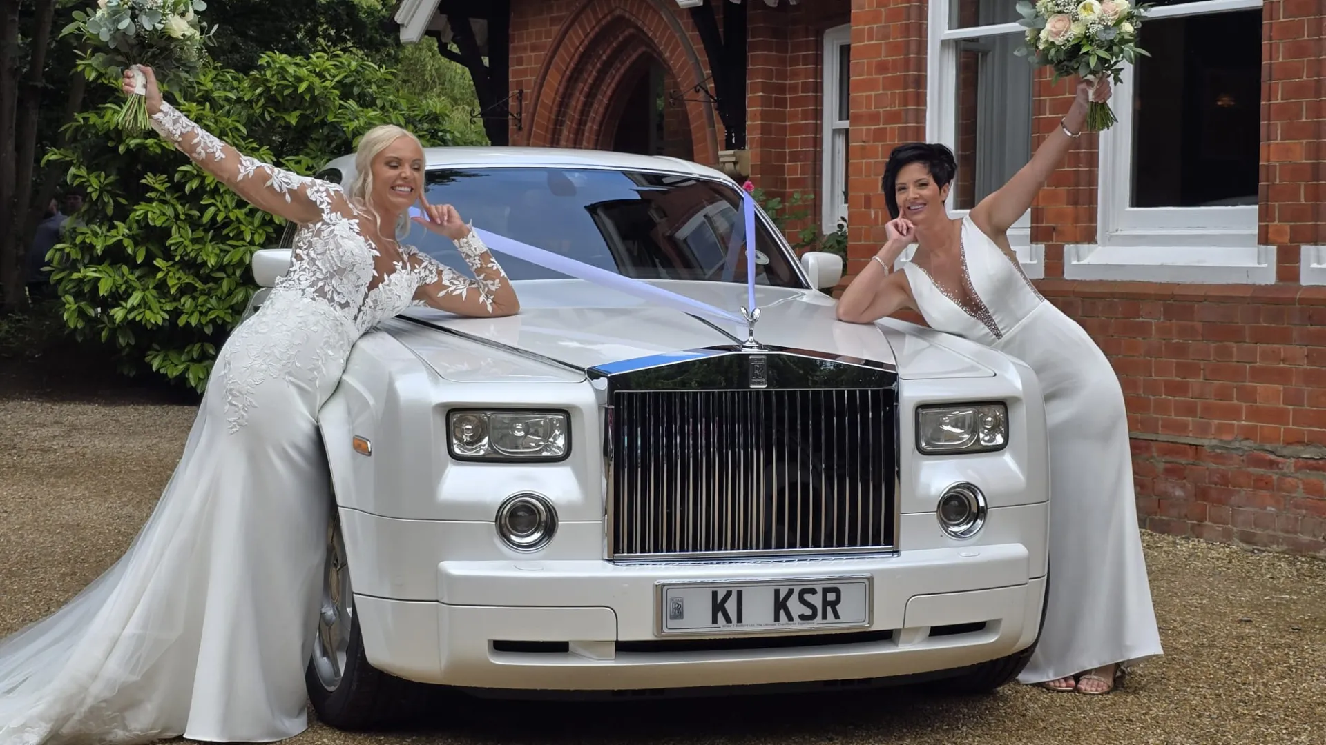 Two Brides in their white wedding dress leaning on the bonnet of a White rolls-Royce Phantom dressed with White Ribbons