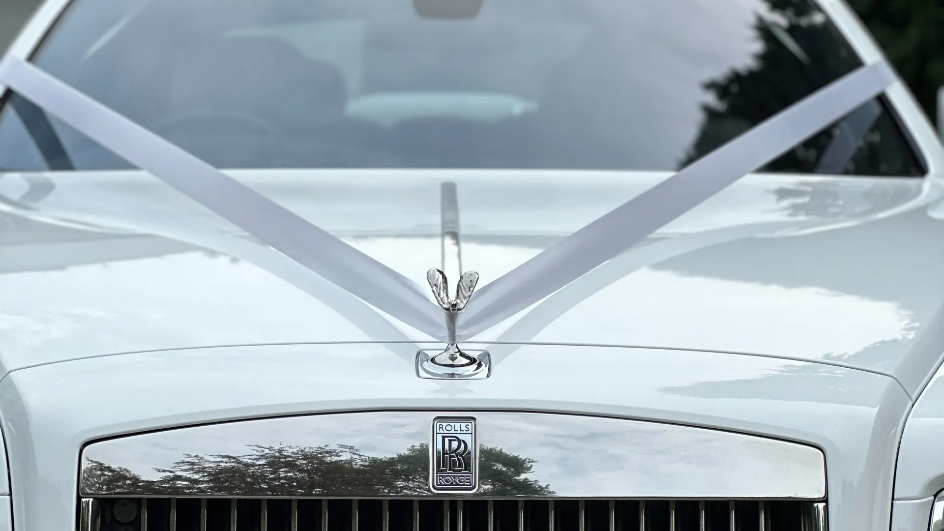 Front bonnet vie of Rolls-Royce Ghost with white traditional V-shape ribbons accross the spirit of Ecstasy.