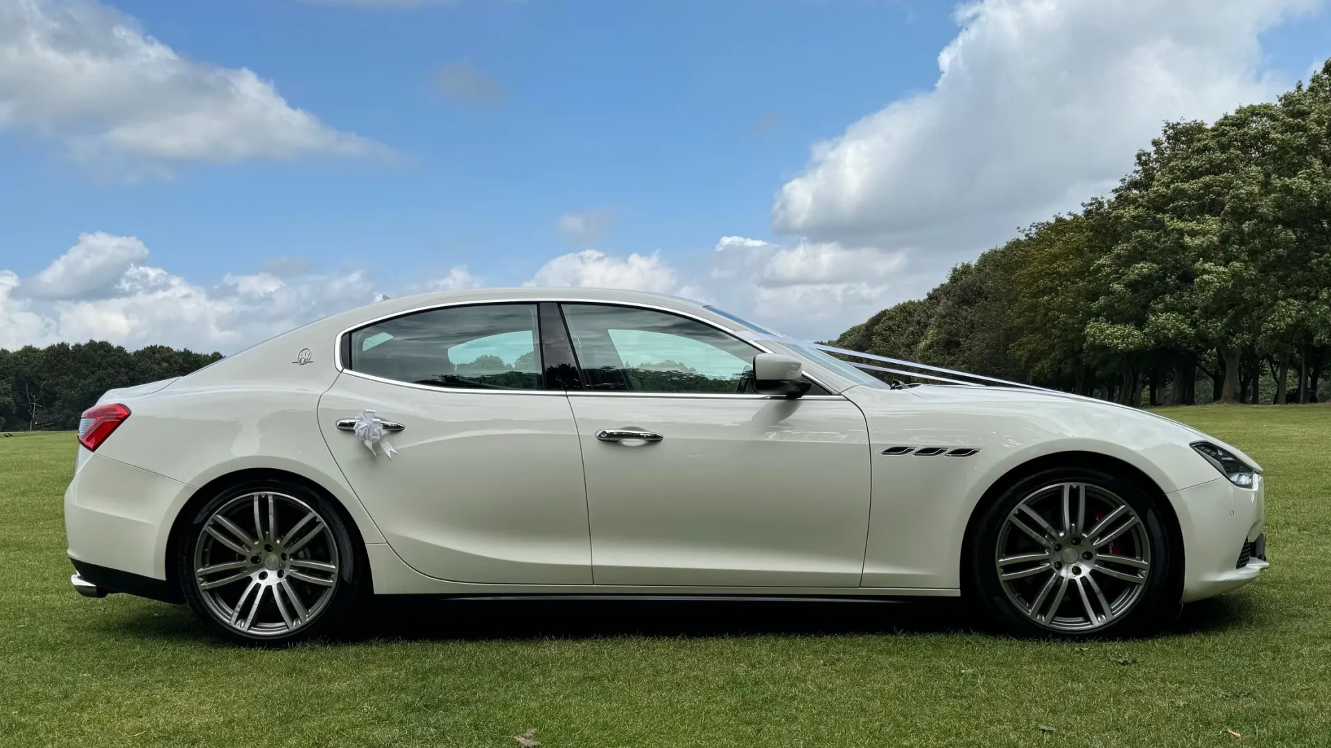 Right side view of white maserati with white bow on rear door handle and chrome alloy wheels