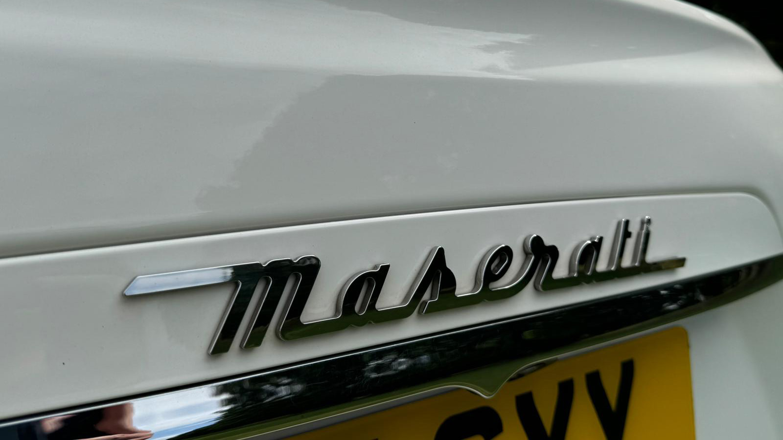 Chrome Maserati logo above the number plate of white maserati ghibli