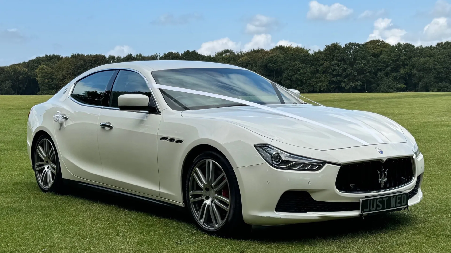 Front right side view of white maserati dressed with with ribbons and bows on door handles