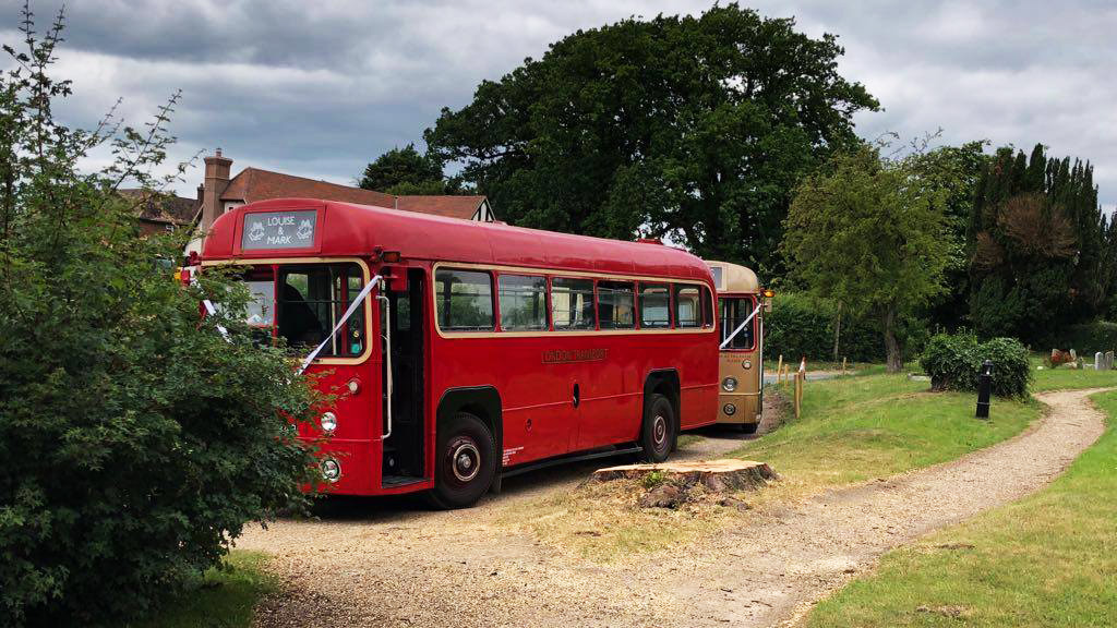 Red single decker bus in front of wedding venue followed by a gold Single Decker bus