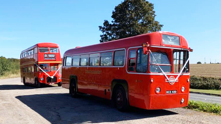 Red Single Decker bus with white ribbons followed by a Red Double Decker bus