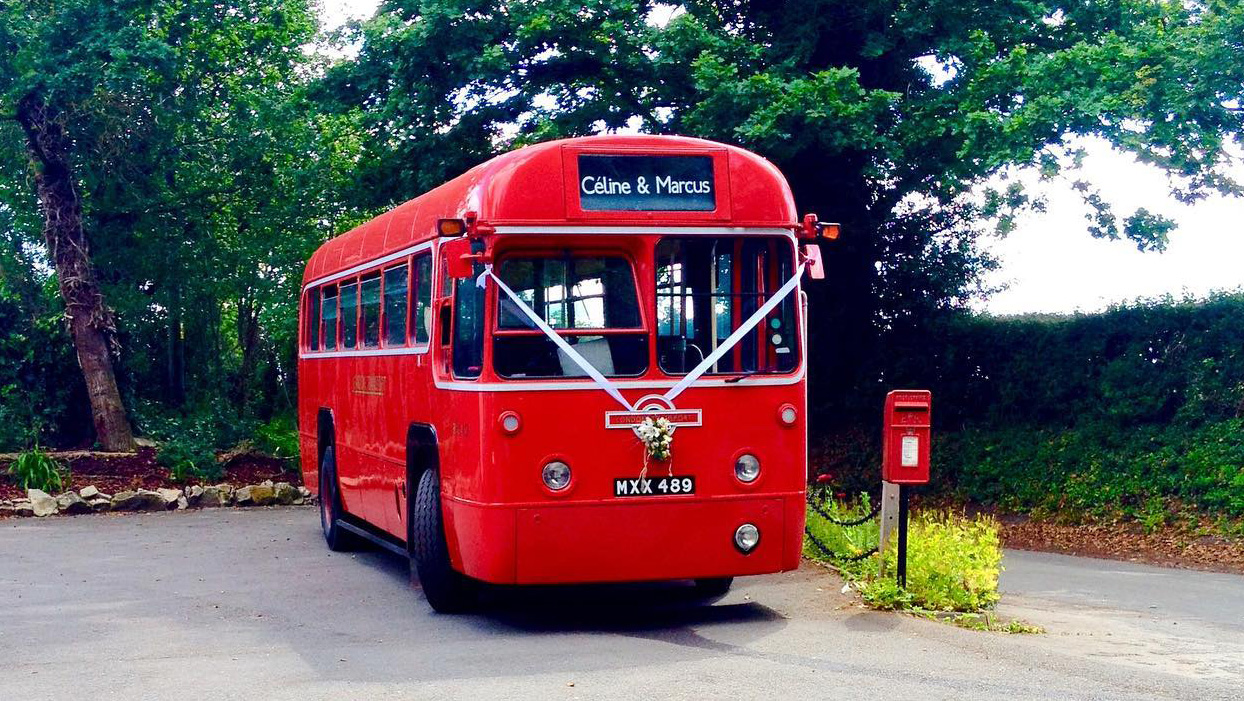 Front view of red classic single decker bus dressed with white ribbons parked next to a red post box.