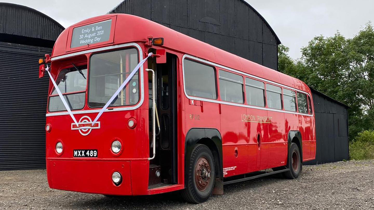 Left side front view of Single Decker Red Bus with white wedding ribbons and front door open