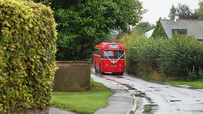 Vintage single decker red bus driving through the Buckinghamshire countryroads