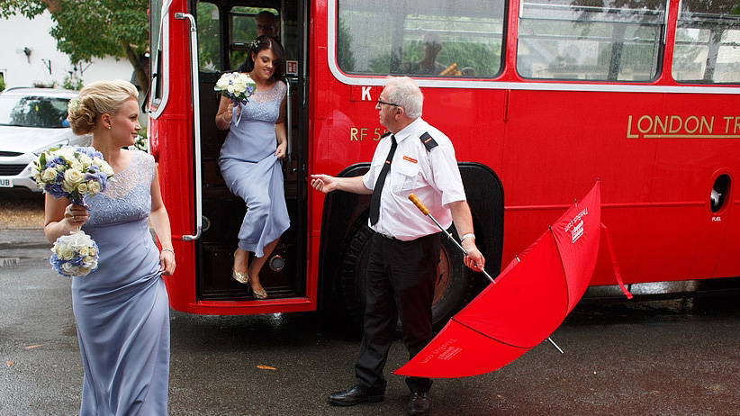 Bridesmaids wearing a light purple dress stepping out of a vintage bus with help from chauffeur