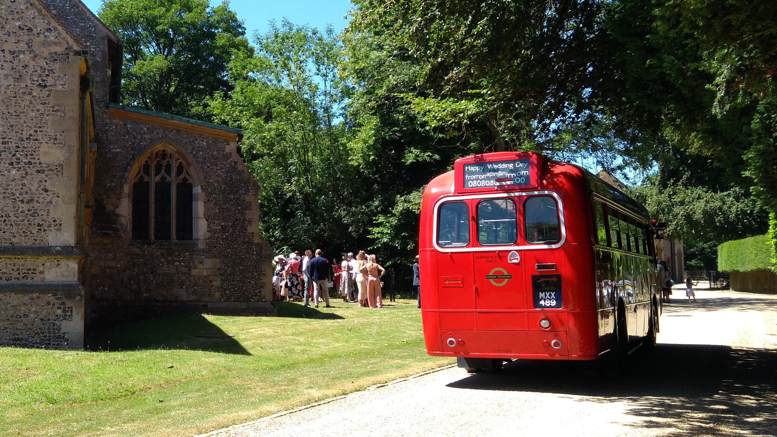 Rear view of Red vintage bus parked next to a wedding church. Wedding guests can be seen in the beackground