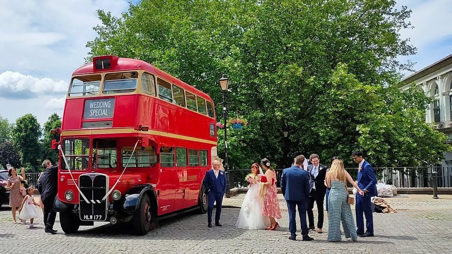 Double Decker Bus decorated with White ribbons parked on front of Hotel venue with wedding guests around the bus