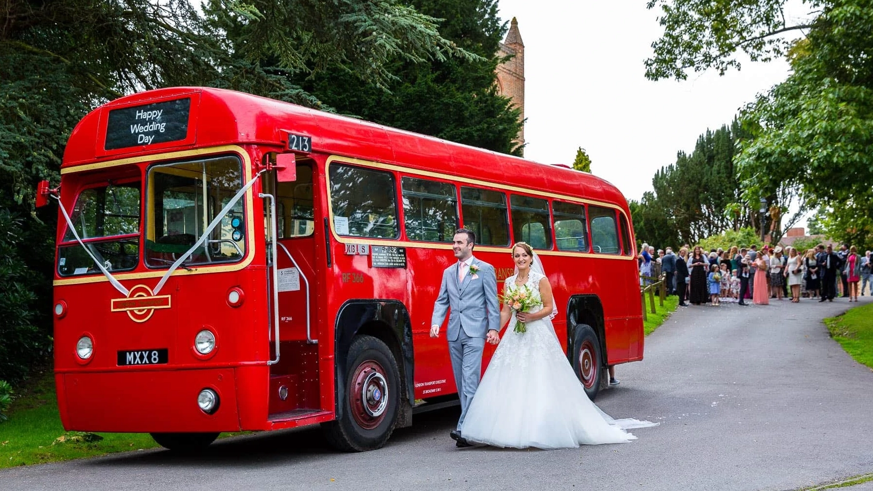 Bride and Groom walking towards the front entrance door of Red Single Decker Bus decorated with white ribbons