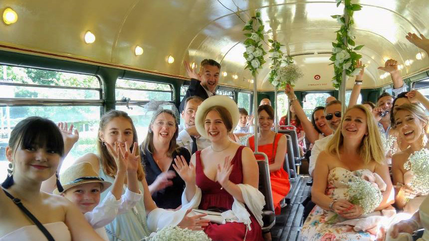 Wedding Party guests seated inside a Classic Single Decker bus smiling and cheering.