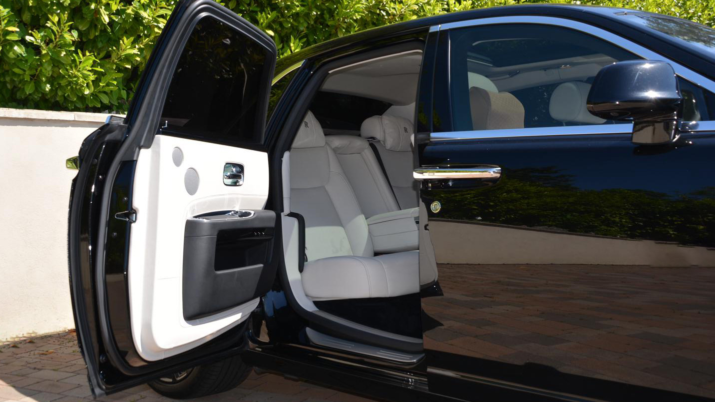 Rear-hinged passenger door open showing white leather interior inside a black Rolls-Royce Ghost