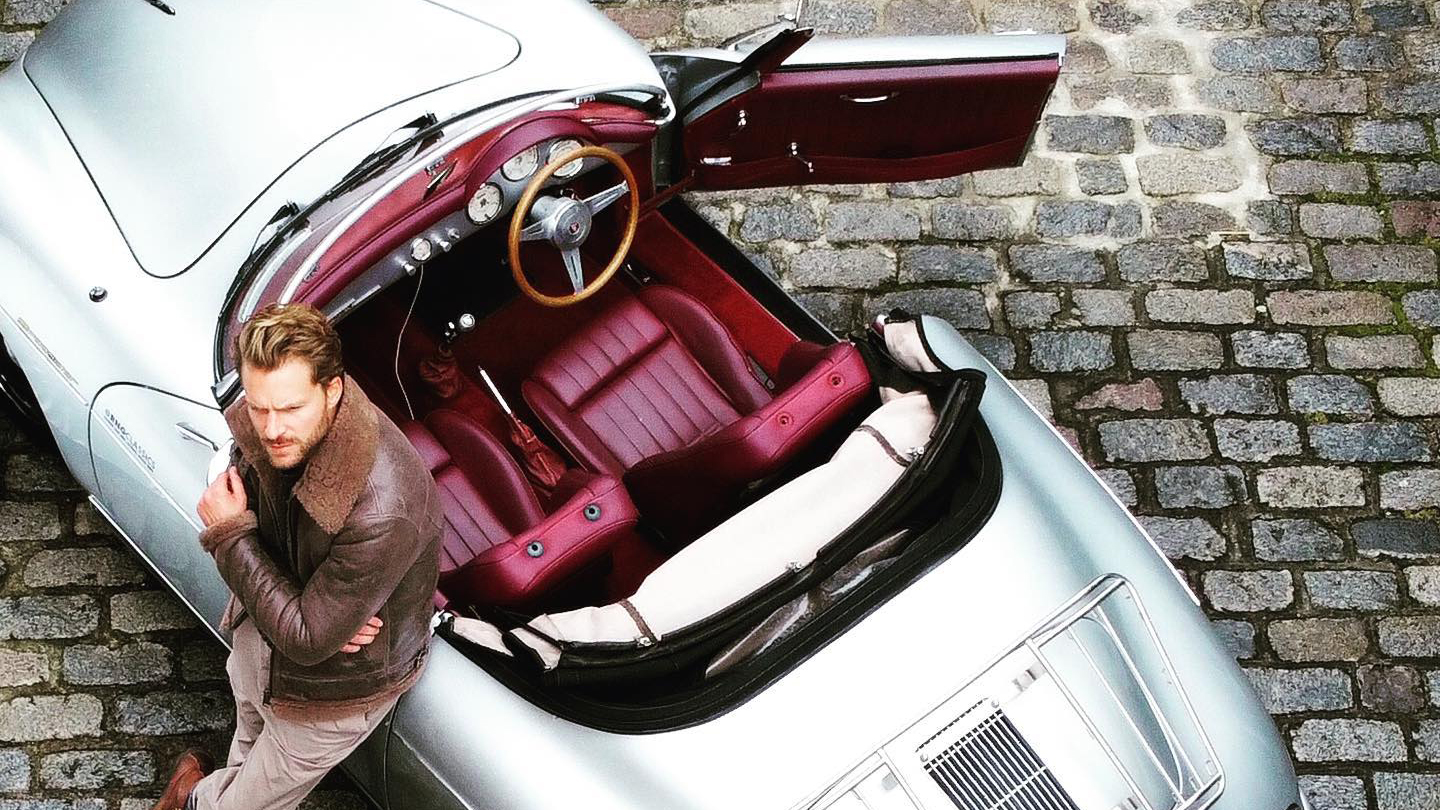 Aerial view of Silver POrsche with convertible roof open showing burgundy leather and driver's door open