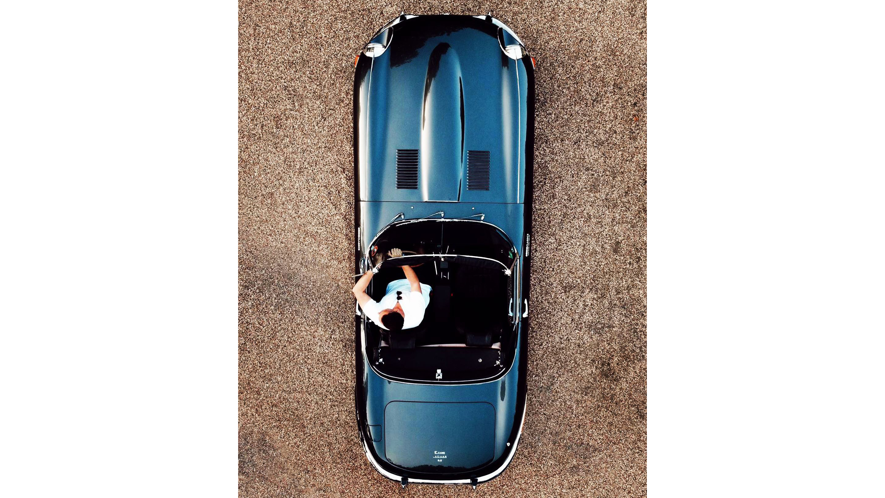 Aerial view of Jaguar e-type with roof open showing black leather interior with chauffeur in the driver seat