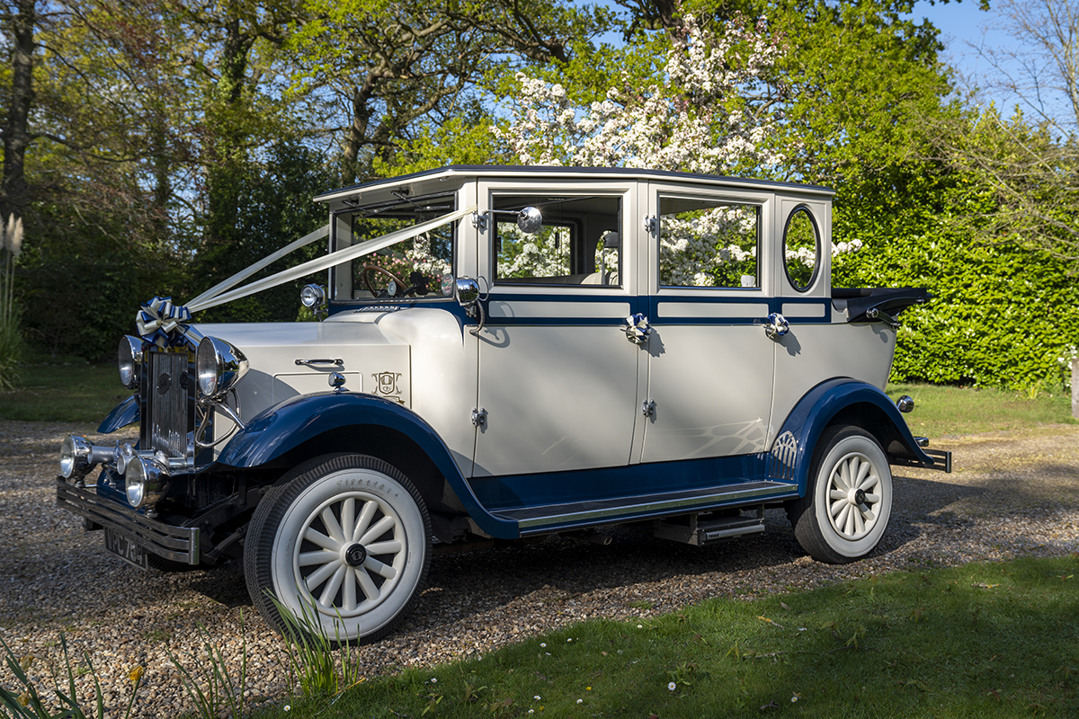 vintage wedding car in ivory and blue decorated with white ribbons and soft-top roof lowered.