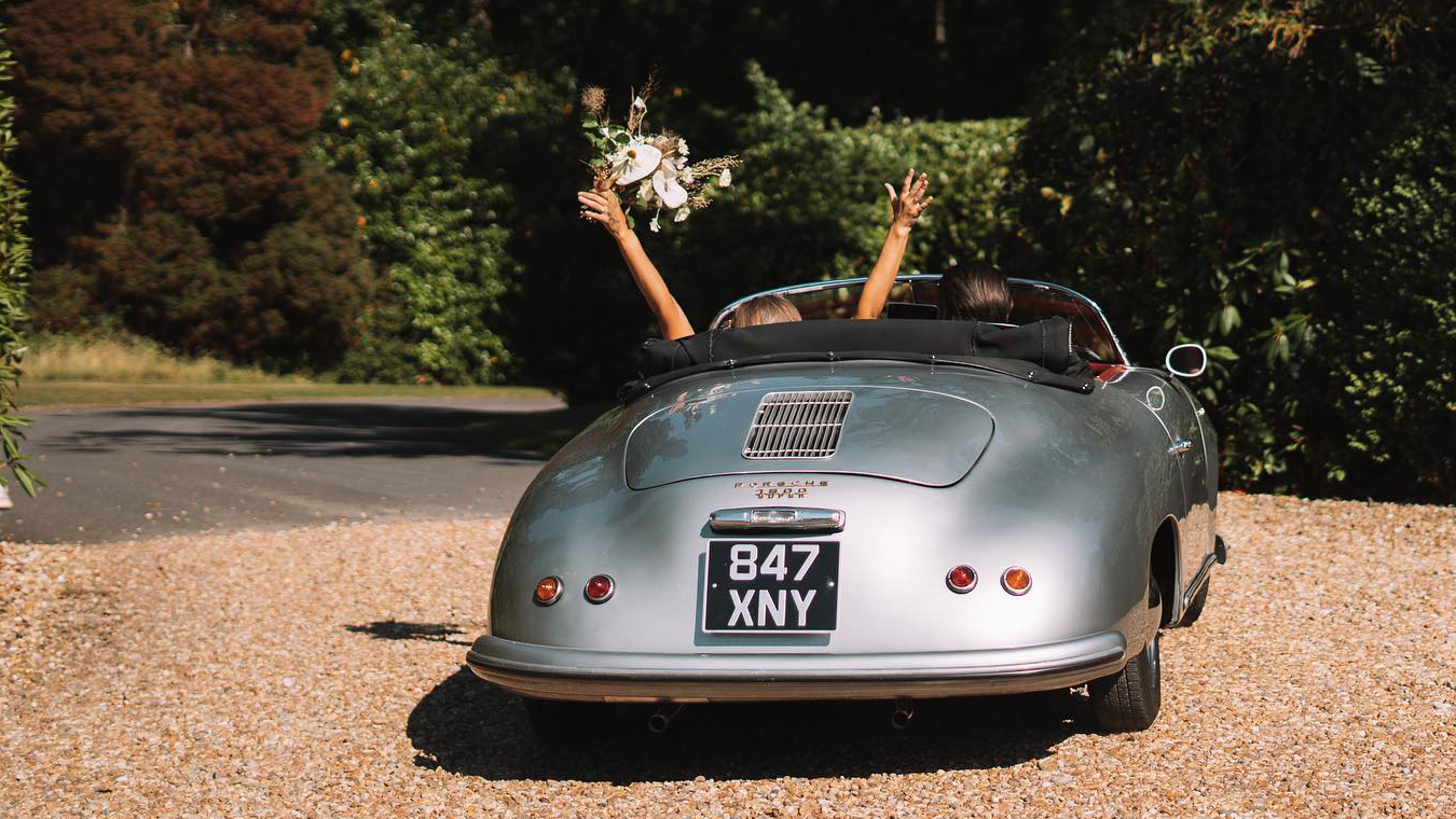 Rear view of classic Porsche with passengers waving inside the vehicle