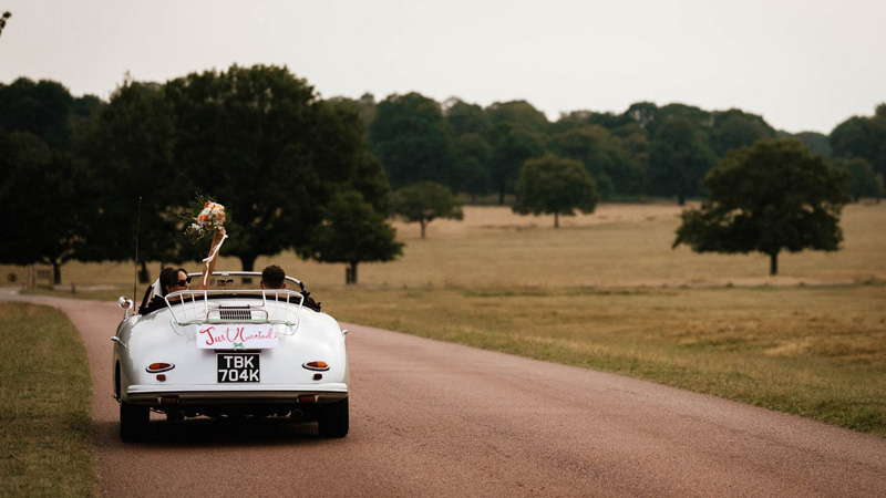 Silver Porsche 356 leaving the wedding venue in Surrey with couple inside the vehicel and "Just Mairried" sign attached at the rear of the vehicle