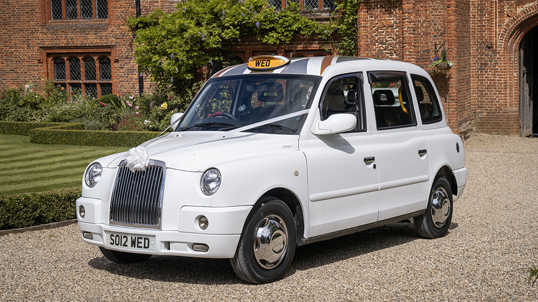 Front left view of white modern taxi cab with wedding ribbons and chrome caps