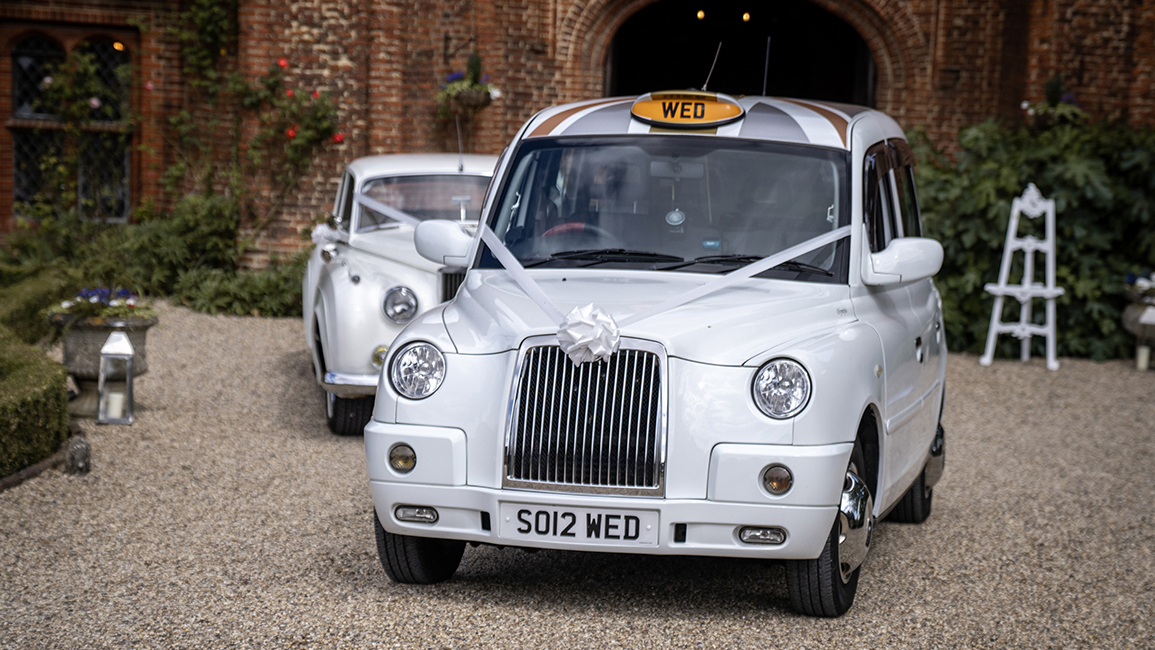 White taxi cab decorated with white ribbons followed by a classic Rolls-Royce