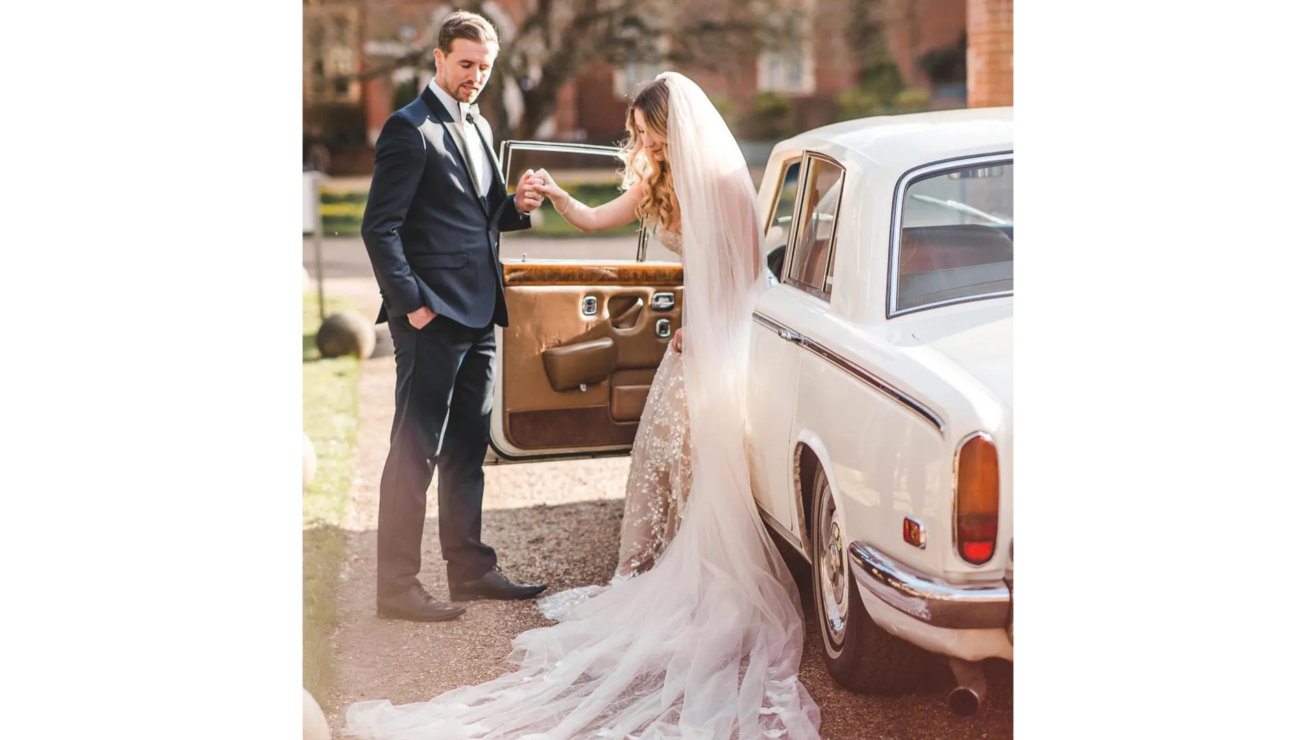 Bride exiting a white classic Rolls-Royce silver shadow with groom holding the door for her.