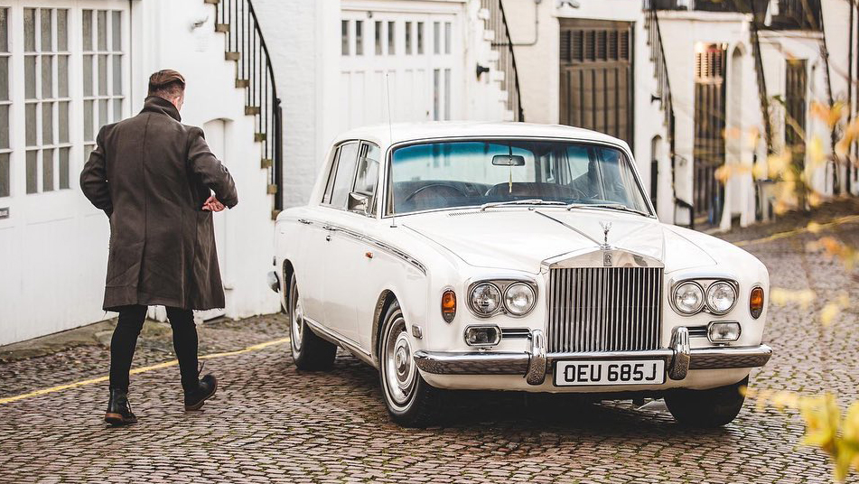 Classic 70s Rolls-Royce in White parked in the street of London for a photoshoot with a male model walking towards the vehicle.