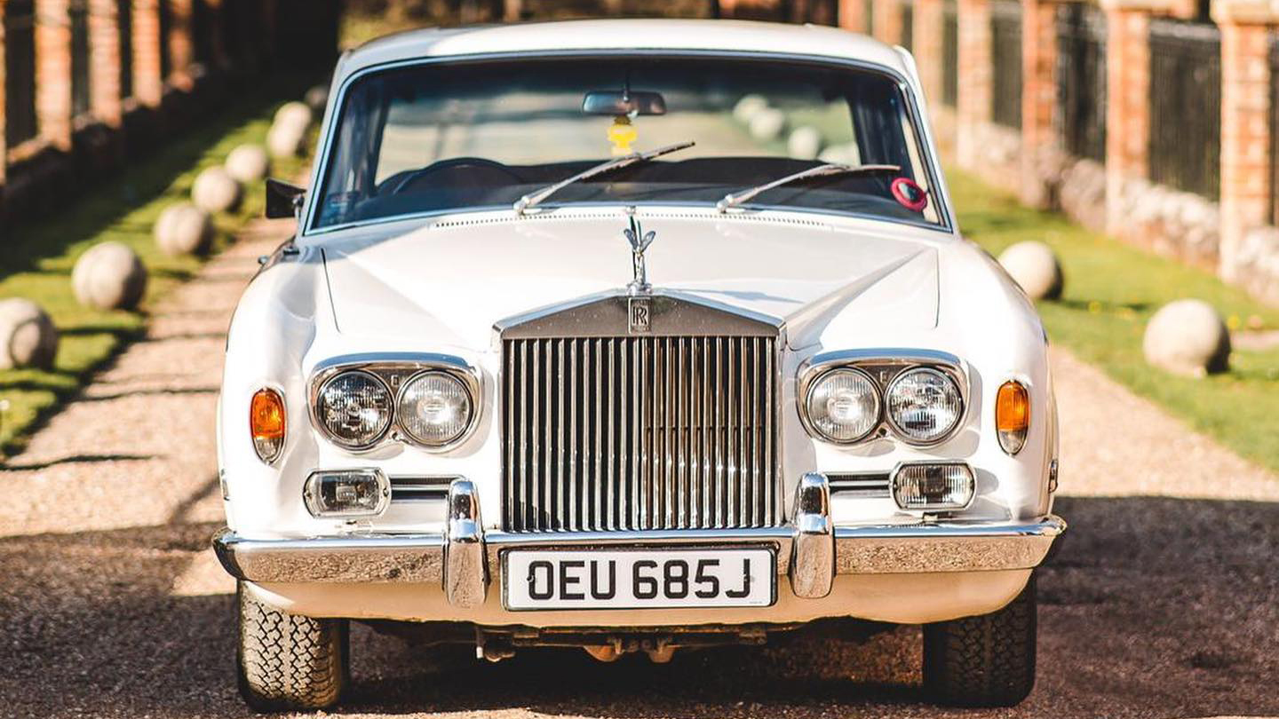 Full front view of Classic Rolls-Royce silver Shadow with twin headlights, orange indicators on the tip of the front wings, large chrome grill with the spirit of ecstasy a top