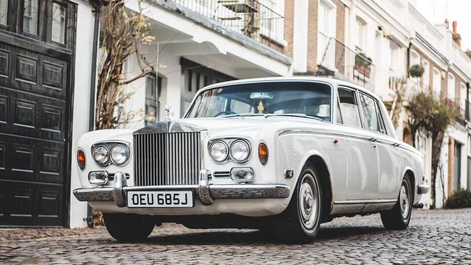 Front view of a 70s Classic Rolls-Royce Silver Shadow in white parked in the street of London showing twin headlight and iconic chrome grill