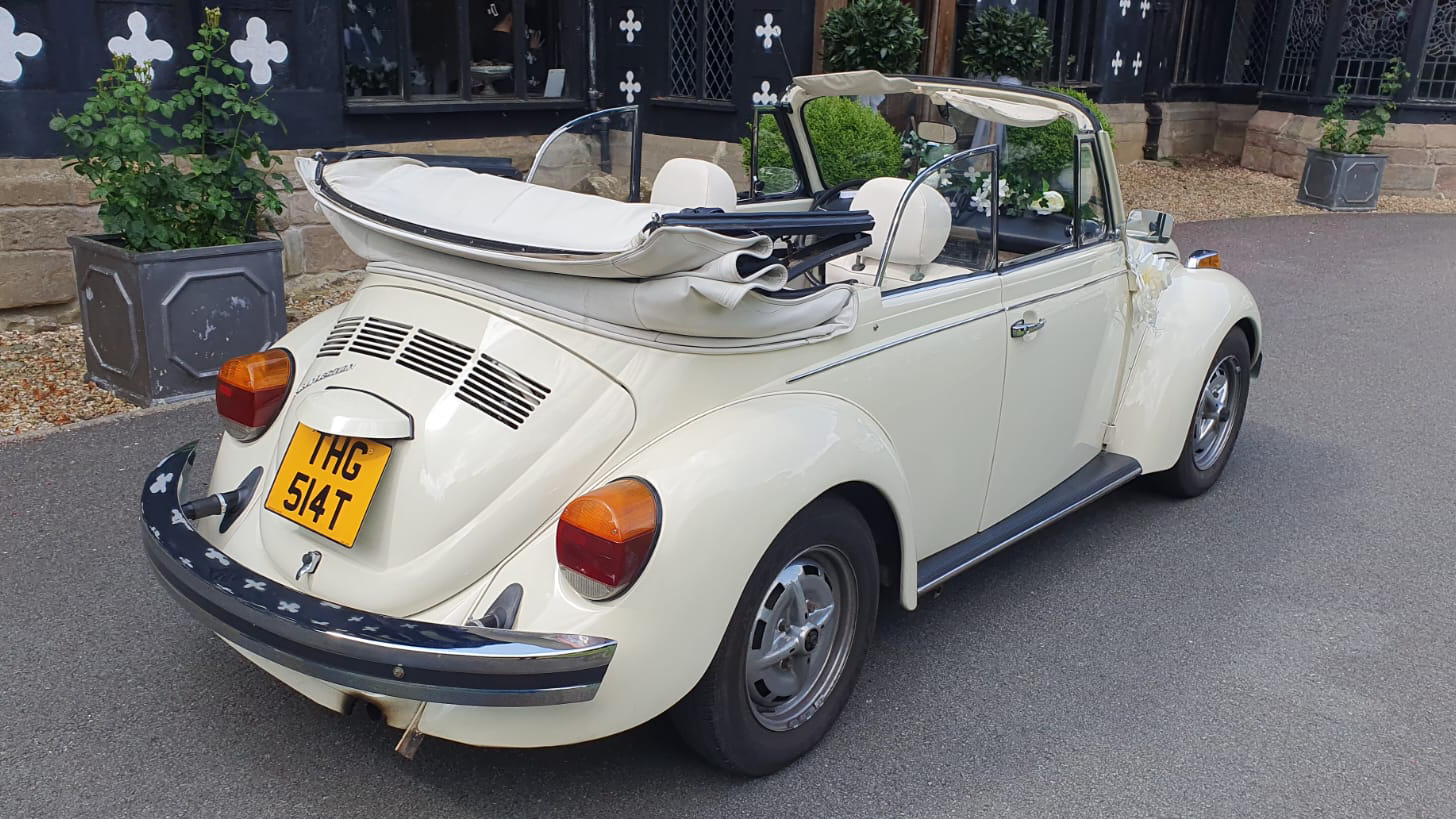 rear side view of classic volkswagen beetle with soft top roof open and covered with a cream cover in front of a wedding venue in Lancashire