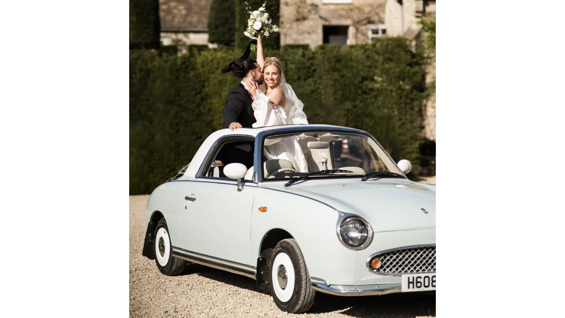 Newly married couple standing inside a Nissan Figaro