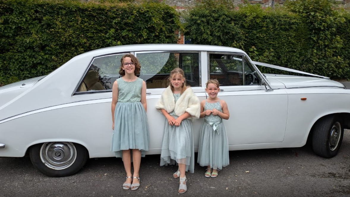 Three flower girls standing in frotn of a White classic Daimler Limousine