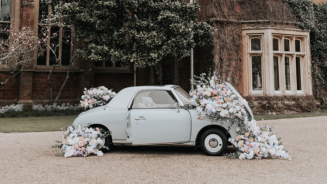 Classic Nissan Fidaro in Power Blue decorated with large flowers in frotn of a wedding venue in Berlshire