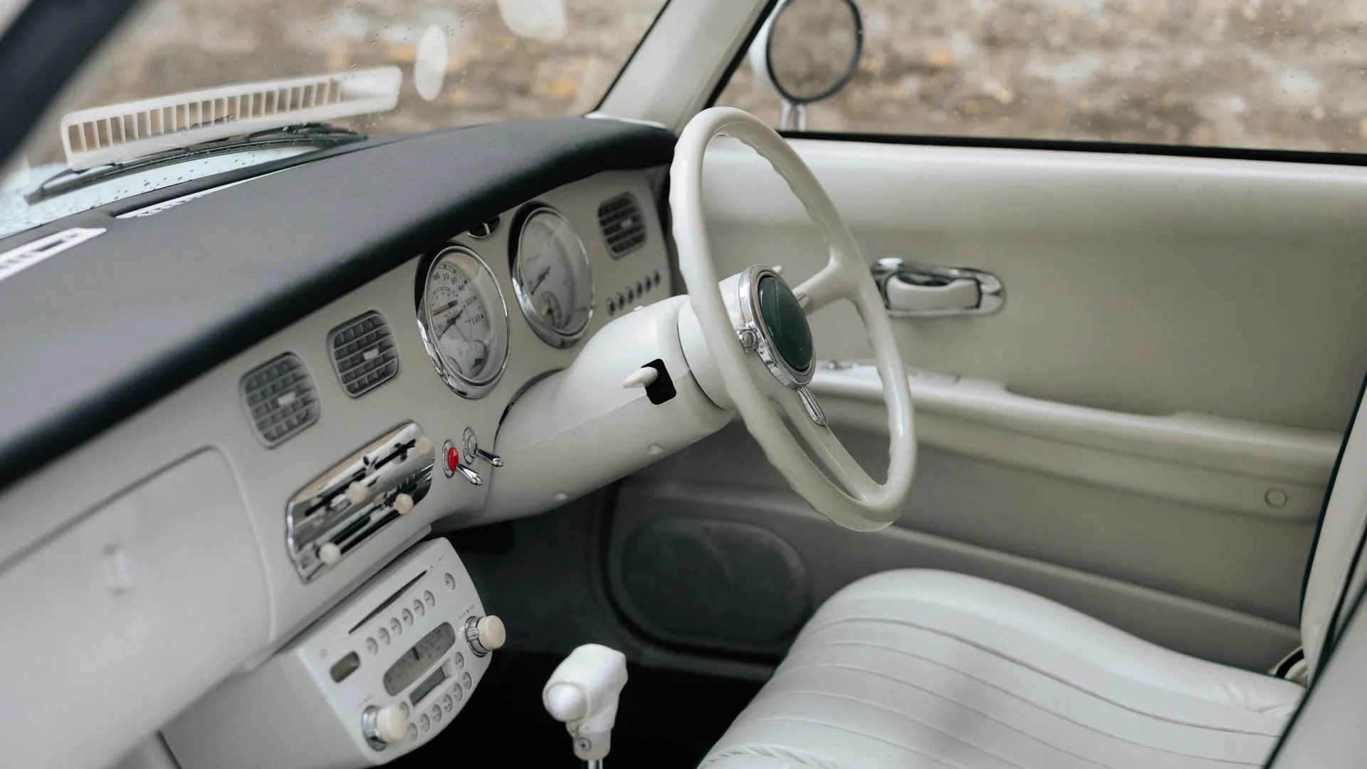 Front driver seat inside Classic Nissan Figaro with white seats, white steering wheel and white dashboard