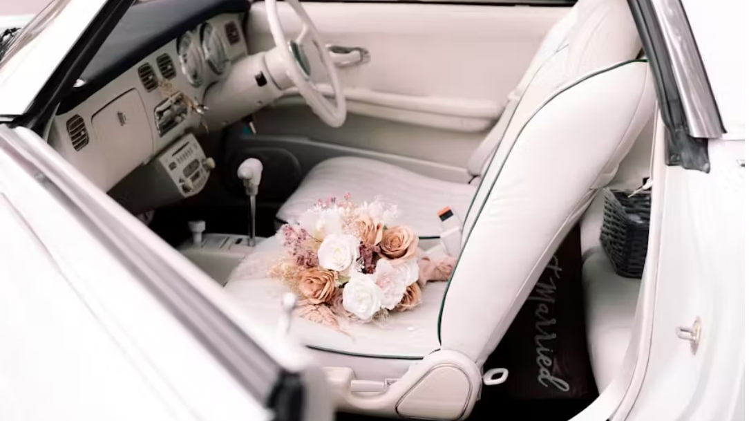 interior photos of Nissan Figaro with white seats. Bunch of colourful flowers layed on the front passnger seat