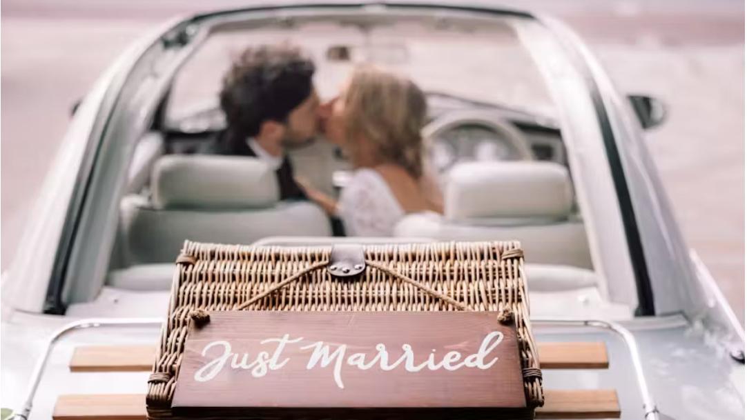 Bride and Groom kissing inside Nissan Figaro with soft top pen and "Just Married" sign attached at the rear