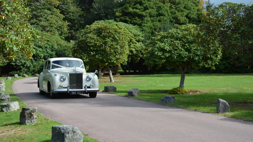 Classic Rolls-Royce silver Cloud decorated with Ivory ribbons driving on the long path leading to the main entrance of Chilsworth Manor in Southampton