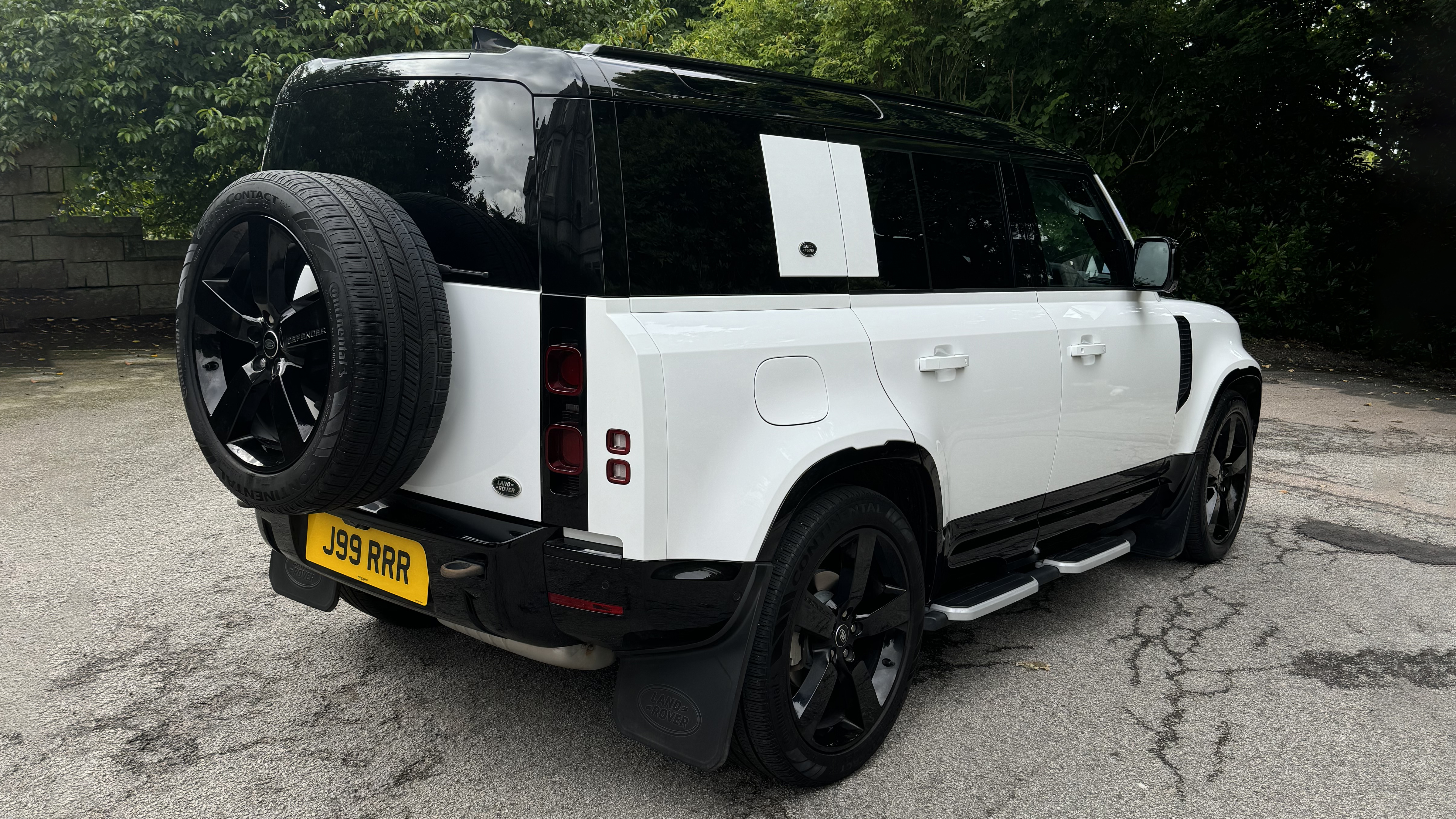 Rear Right side view of White Land rover Defender with Black Roof and Large Black Alloy wheels attached to rear boot